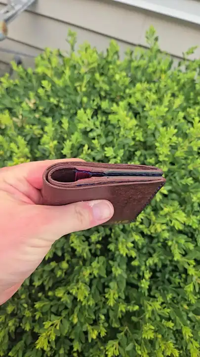 Folded oxblood bifold, edge on, out by the hedge — Rogue Artisan, East Vancouver